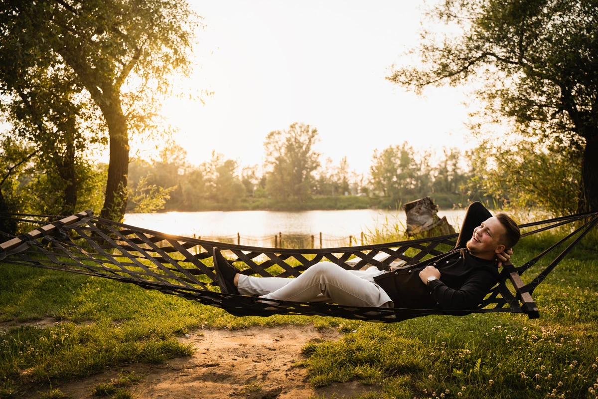 młody uśmiechnięty mężczyzna odpoczywa na hamaku w świetle zachodzącego słońca nad jeziorem