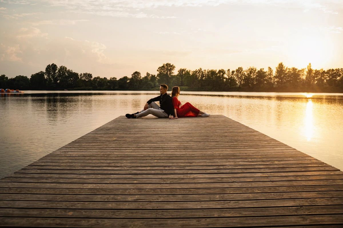 Para siedząca na molo nad jeziorem w mroku zachodzącego słońca